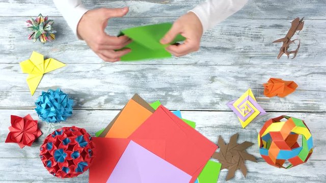 Torning green paper by hands. Folding colorful paper while making origami figures. Top view, flat lay.