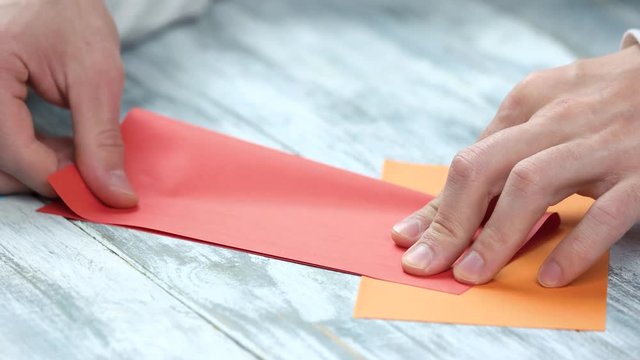 Folding red paper, close up. Male hands making origami, bending and smooting red paper sheet.