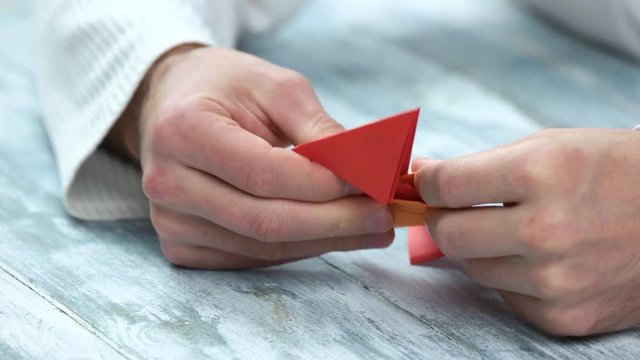 Crafting origami figure with red and orange papers. Male hands making origami, close up.
