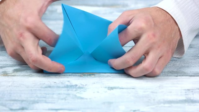 Crafting origami figure with blue paper. Male hands, folding and bending colourful paper sheet.