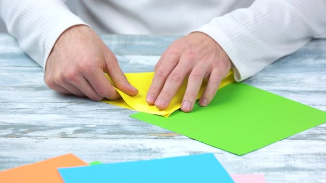 Making origami with yellow and green paper. Male hands folding paper.