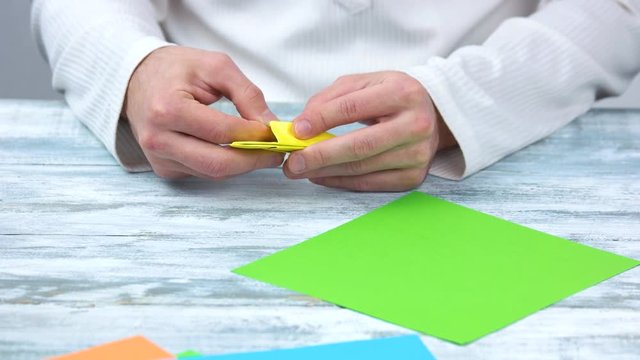 Folding paper, creating origami figure. First step of making yellow origami flower, close up.
