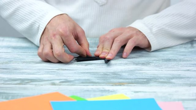 Man making origami with black paper. Close up. Mal hands creating origami figure.