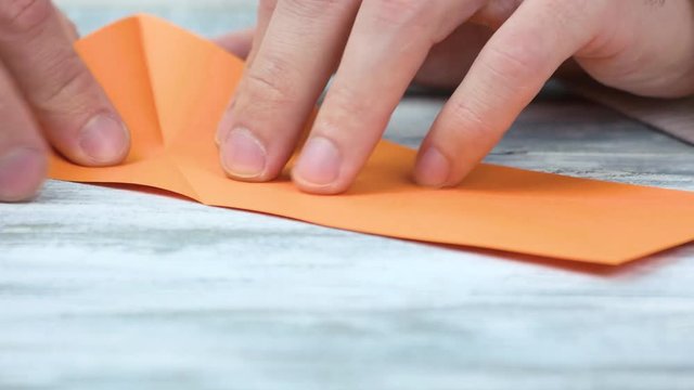Creating origami, close up. Male hands and orange paper.