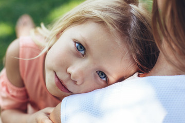 Waist up portrait of peaceful small girl lying on mother shoulder. She is calm and serene enjoying...