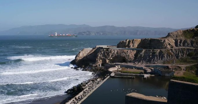 Time lapse of Sutro Baths on a sunny spring morning.  Surf rolls in from the Pacific.  Sea gulls bath on the remains of the swimming pool.  A large ship steams by.  Clear blue sky.
