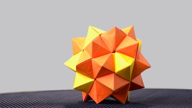 Orange origami sharp ball exposition. Polygon shape form sphere rotating. Grey background.