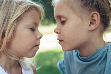 Make a wish. Profile of two sisters turning to each other with closed eyes. They are playing outdoors enjoying summer together
