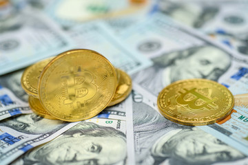 A bunch of gold bitcoin coins laying over hundred dollar bills background 