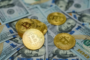 A bunch of gold bitcoin coins laying over hundred dollar bills background 