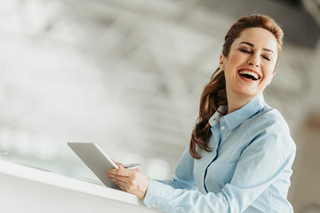 Portrait of laughing female employer with attractive smile and closing eyes using digital device...