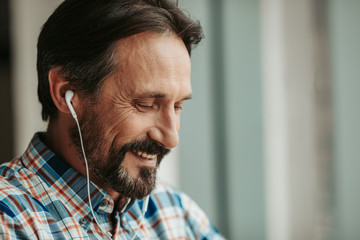 Portrait of bearded cheerful man with attractive smile listening music in headphone. Copy space