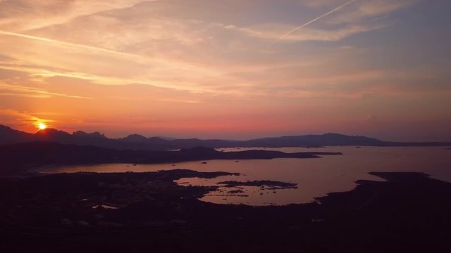 Video from above, aerial view of an amazing sunset behind some hills and a coast bathed by the Mediterranean Sea in Sardinia, Italy.