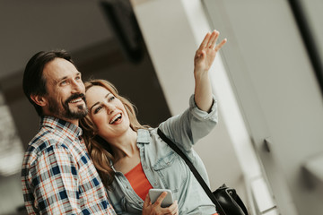 Portrait of happy bearded male hugging cheerful female. She gesticulating hand and holding mobile....