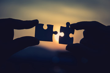 Two hands trying to connect couple puzzle piece with sunset background. Jigsaw alone wooden puzzle...