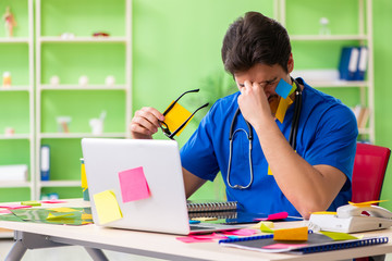 Young doctor sitting in hospital with many conflicting prioritie