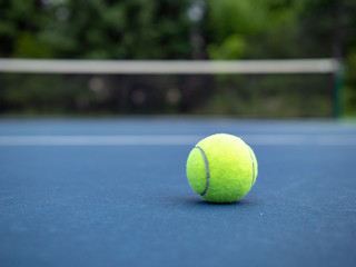 Grounded tennis ball sitting on ground with court net in background 