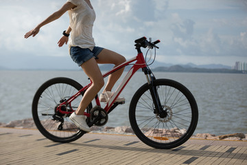 Free woman riding a bike on sunny seaside with arms outstretched