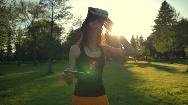 Beautiful caucasian woman enjoy virtual reality walking on grass in park. VR headset glasses device. nature outdoors background. people and technology concept. Sunset or sunrise natural lighting.