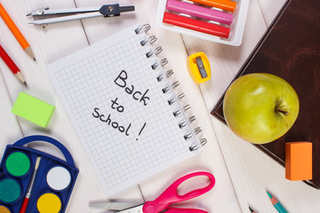 Book and school accessories on white boards, back to school inscription in notepad
