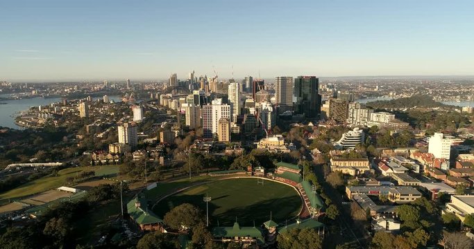 St Leonards park of green lawns, sports fields and oval facing tall high-rise towers and distant Sydney city CBD.
