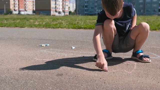 Boy draws with blue chalk on the asphalt. Close-up hands.
