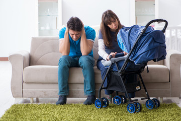 Young parents with their newborn baby in baby pram sitting on the sofa 