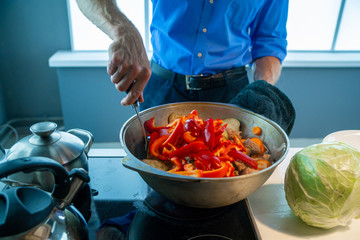 A man prepares a stew of meat and vegetables, stirs in a saucepan of Bulgarian pepper.