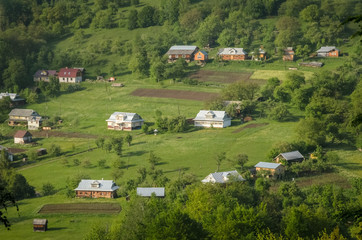 Scenic shot of rural area at mountains taken at sunny spring day. Remote houses are scattered on the slope of the hill covered with forest and meadows. Concept of clear environment. Natural background