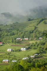 Scenic shot of rural area at mountains taken at sunny spring day. Remote houses are scattered on the slope of the hill covered with forest and meadows. Concept of clear environment. Natural background