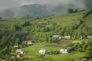 Scenic shot of rural area at mountains taken at sunny spring day. Remote houses are scattered on the slope of the hill covered with forest and meadows. Concept of clear environment. Natural background