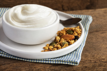 Healthy flavored yogurt in ceramic bowl with cereal and granola on cloth with wood background with copy space for your text.