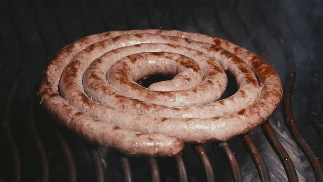 Slow motion shot of the delicious homemade meat sausage frying on the grill with flames and smoke