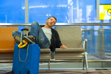 lifestyle portrait in airport of young attractive and tired tourist man with suitcase sleeping at...