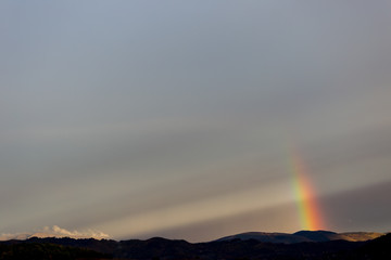 Beautiful and surreal view of part of a rainbow over some hills