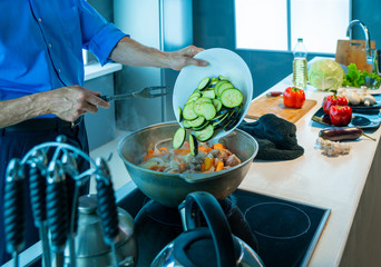 The man is cooking food. Lay eggplants in a pot