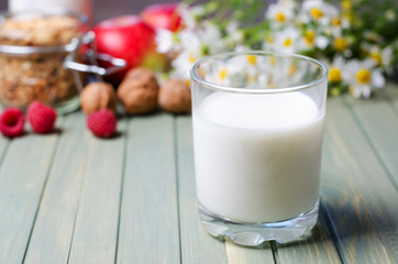 The concept of a healthy diet. Milk in a glass glass Cup on a wooden background. Background-nuts, red apples, raspberries, daisies.