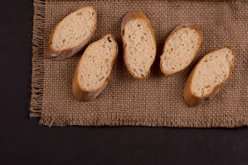 Pieces of sliced ​​baguette  lie on a dark jute napkin on dark table.
