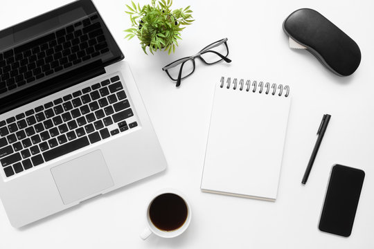 White office desk table with blank notebook, laptop and other office supplies. Top view with copy space, flat lay.