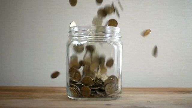 Slow motion, a pile of coins falls into an empty glass jar on a white background. Ukrainian coins fall into a jar.