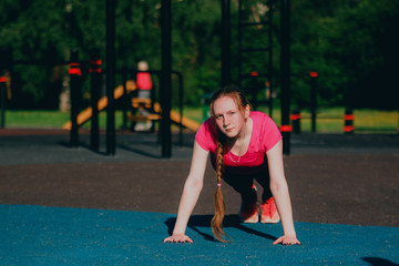 Girl in pink sportswear doing push up exercises at street workout place in summer morning. Healthy lifestyle sport concept.
