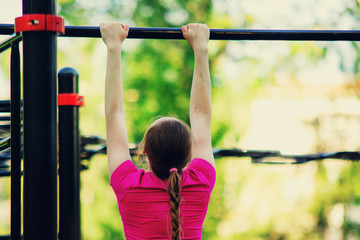 Pull ups on a horizontal bar. Girl in pink sportswear doing exercises at street workout place in summer morning. Healthy lifestyle sport concept.