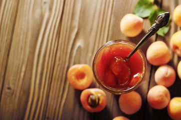 Glass Jar of Apricot jam on wooden table with ripe apricots at background. Top view.