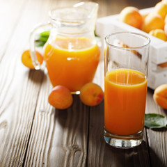 Apricot smoothie in glass on wooden table with crate and jug at background