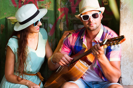 Happy smiling couple in sunglass and hat  with guitar drinking juice spending carefree time together.