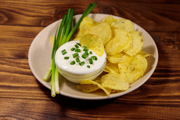 Crispy potato chips with green onion and sour cream on wooden table