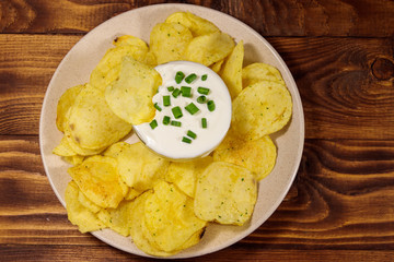 Crispy potato chips with green onion and sour cream on wooden table. Top view