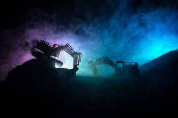 Construction site on a city street. A yellow digger excavator parked during the night on a construction site. Industrial concept table decoration on dark foggy toned background