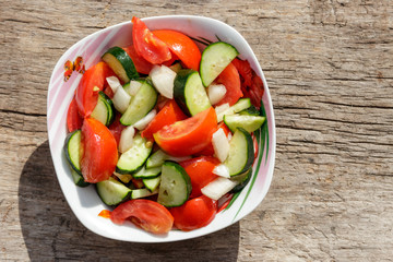 Fresh vegetable salad  with tomatoes, cucumbers, onion and olive oil on wooden table. Top view