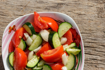 Fresh vegetable salad  with tomatoes, cucumbers, onion and olive oil on wooden table. Top view